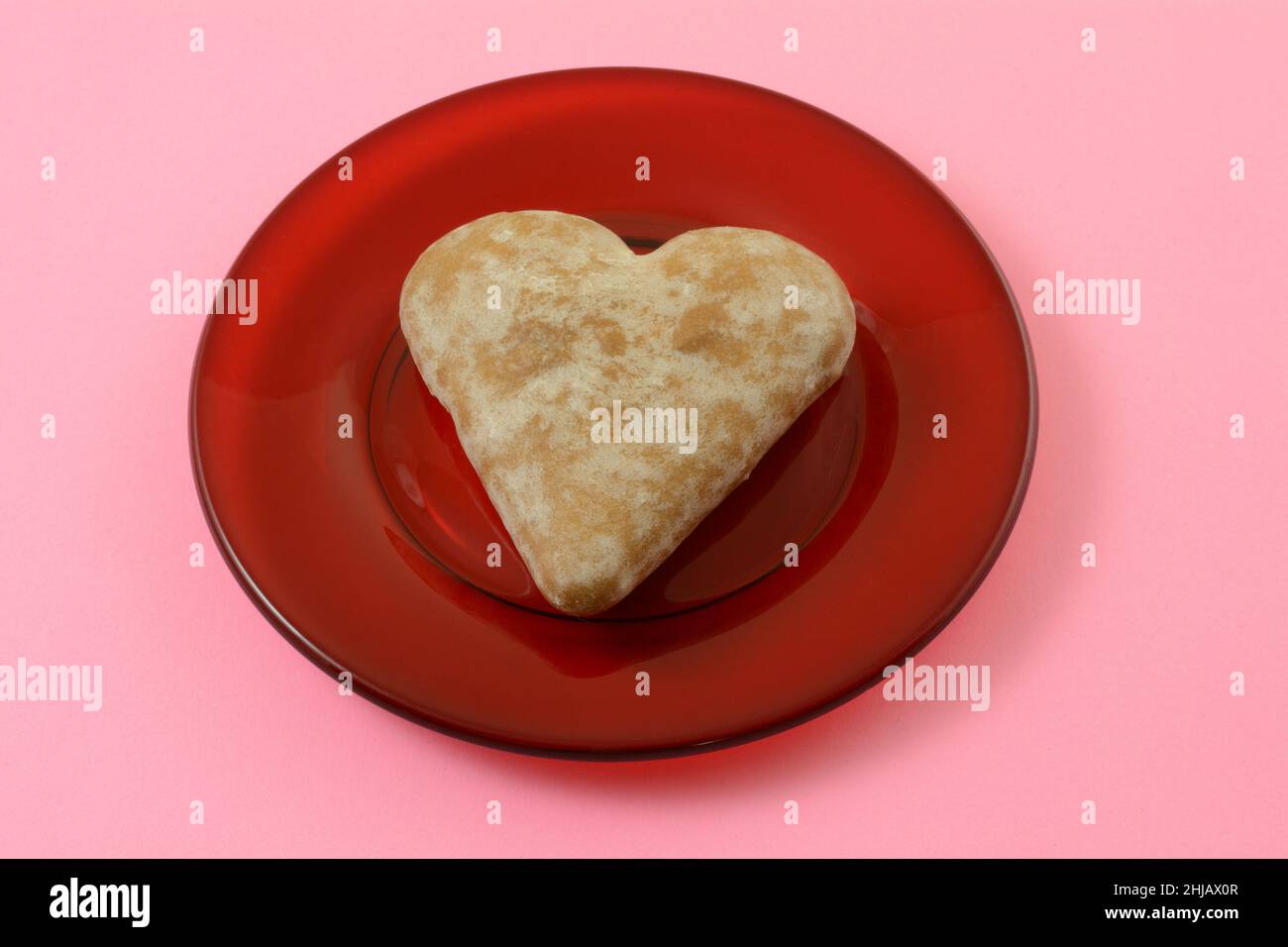 Weiches herzförmiges Ingwerkeks auf rotem Glasplatte auf rosa Hintergrund Stockfoto