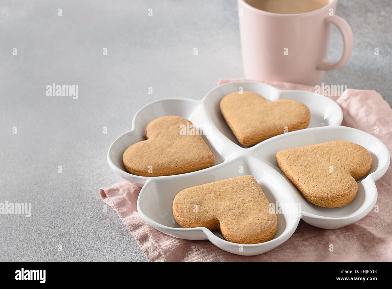 Herzförmige Kekse auf weißem Kombinationsteller zum Valentinstag auf grauem Hintergrund. Blick von oben. Platz für Ihre Grüße. Stockfoto