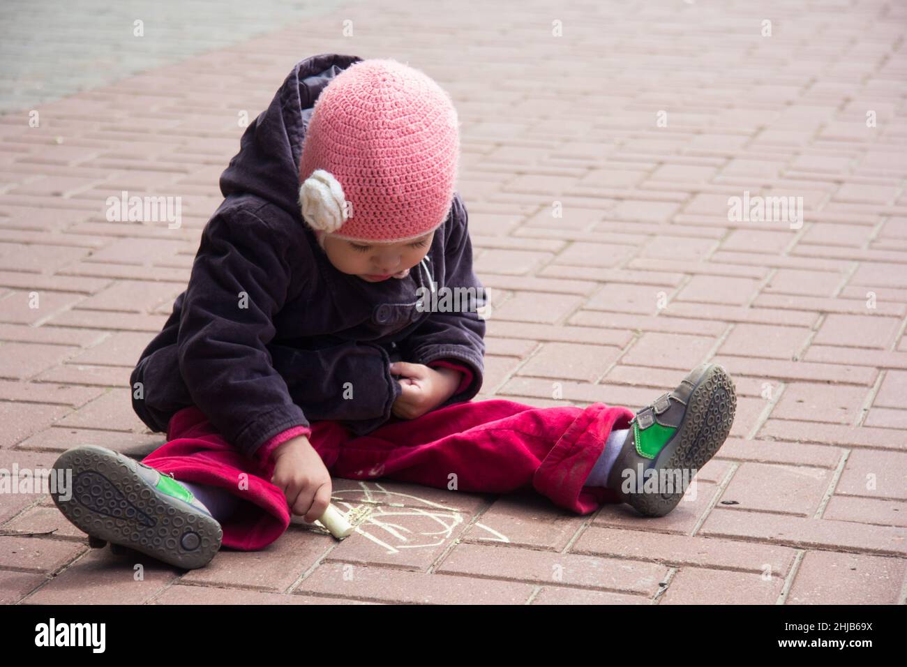 Kaukasisches kleines Mädchen von drei Jahren Zeichnung mit Kreide auf dem Boden im Freien Stockfoto