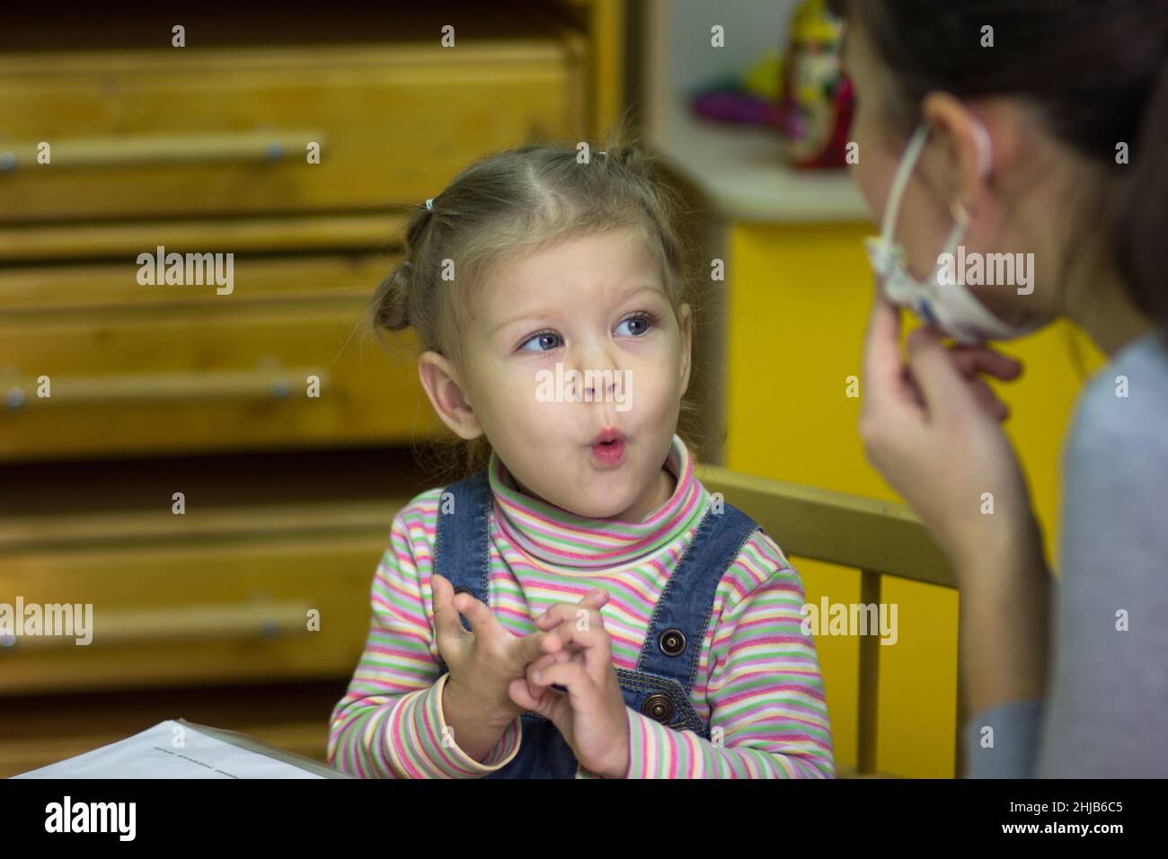 Porträt eines kaukasischen Kindes, das zwei Jahre alt ist und mit dem Lehrer mündliche Übungen macht und nach ihr wiederholt Stockfoto