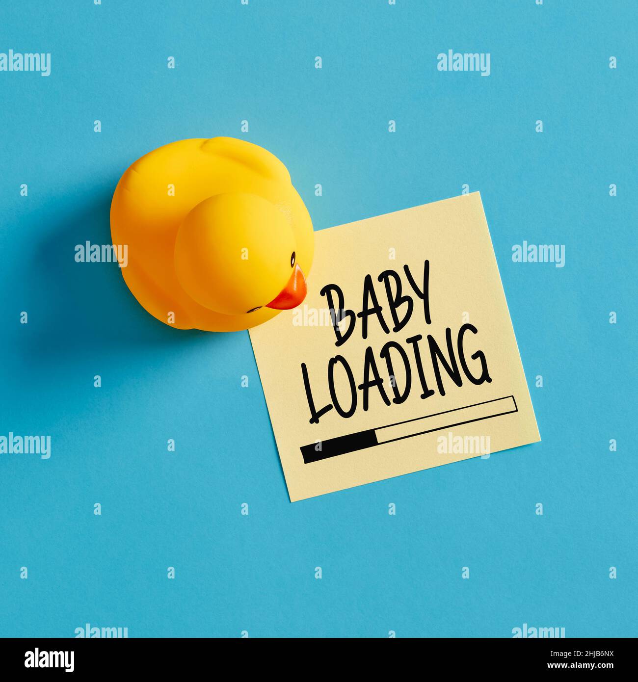 Babyladung Nachricht geschrieben auf einem gelben Haftnotiz mit einem Gummi Ente Spielzeug auf blauem Hintergrund. Stockfoto