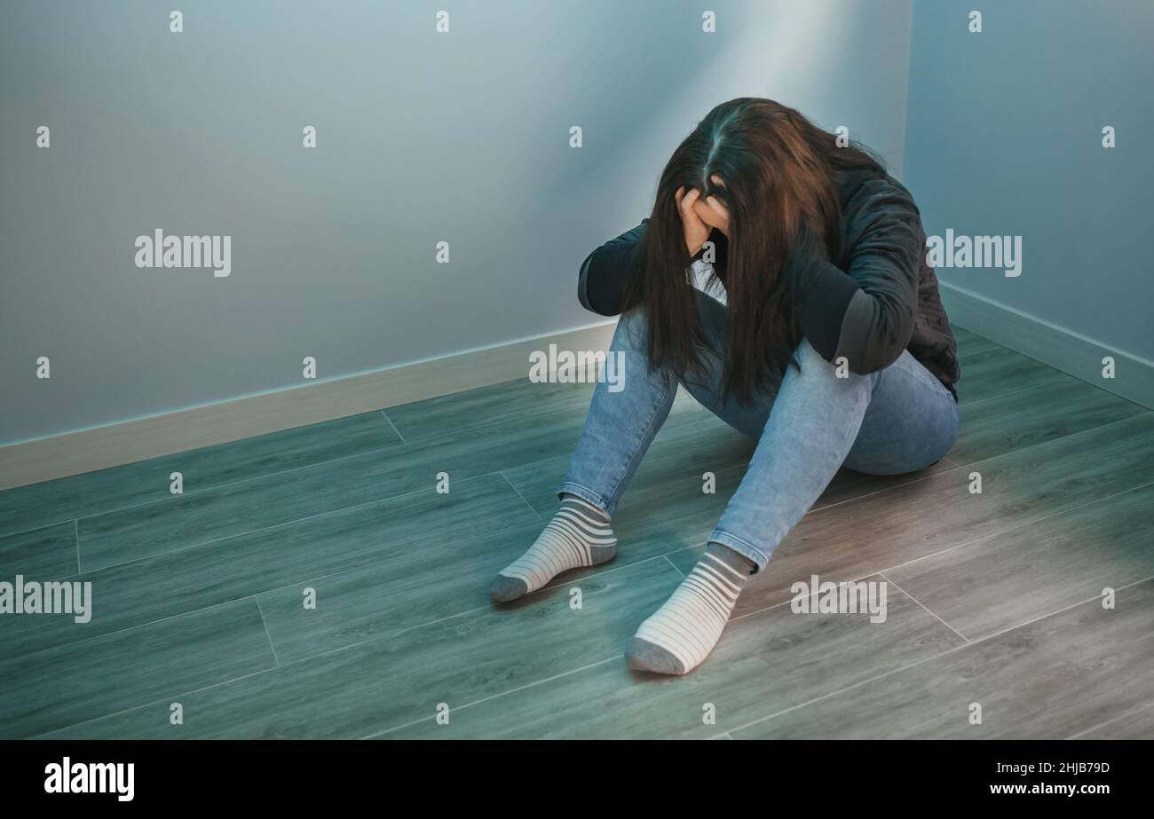 Frau mit psychischen Problemen mit Händen im Kopf auf dem Boden sitzend Stockfoto