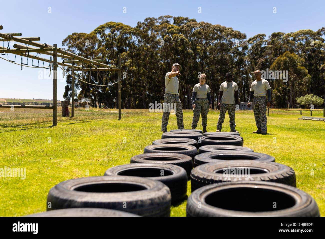 Männlicher Instruktor, der eine Gruppe männlicher und weiblicher Soldaten für den Reifenpanzer-Parcours im Bootcamp instruiert Stockfoto