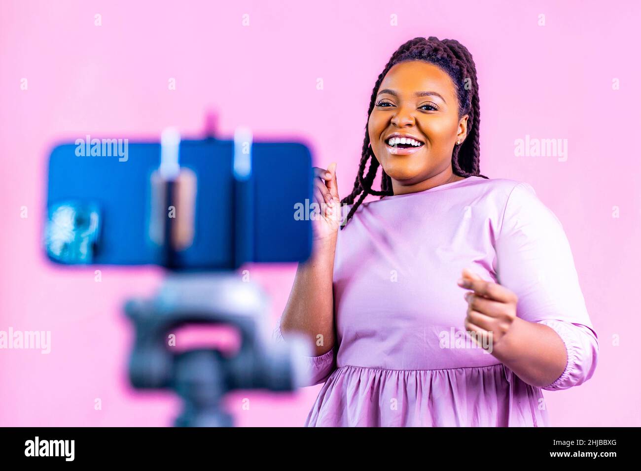 Dunkelhäutige Frau, die lachend und Social-Media-Geschichten auf pinkem Wandhintergrund gedreht hat Stockfoto