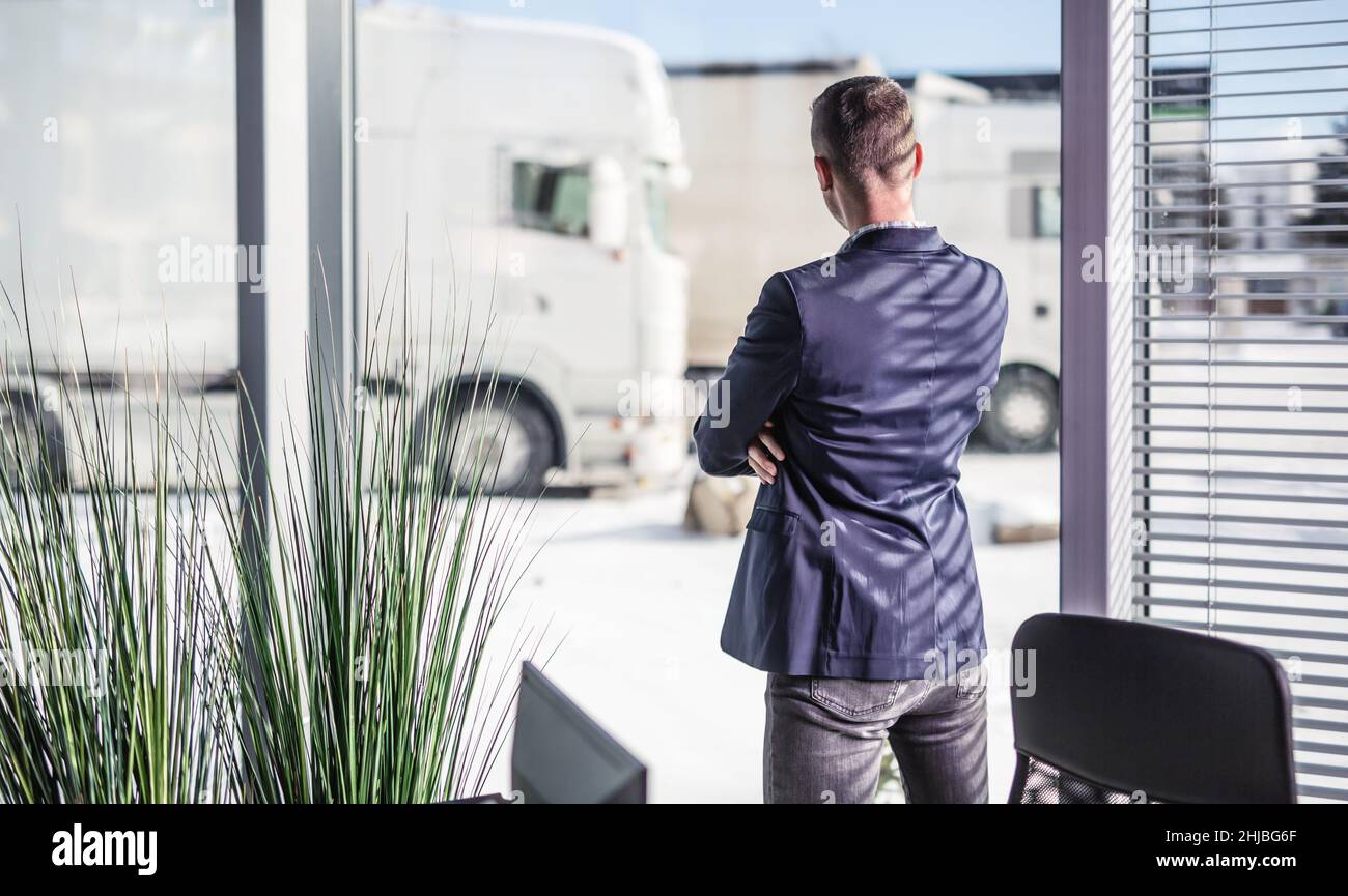 Der Manager der Spedition schaut aus dem Fenster und der Flotte geparkter Lastwagen, während die Lkw-Fahrer knapp werden. Stockfoto