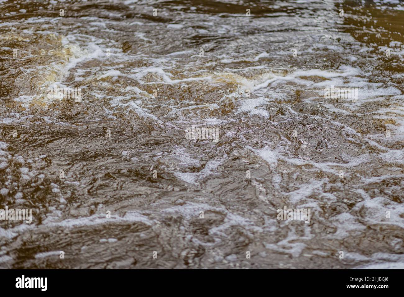 Wasser eines Flusses, turbulent, die schnell fließen, Wellen bilden und Schaum verursachen, ist der Fokus in der Mitte mit dem Rest und der Hintergrund verschwommen Stockfoto