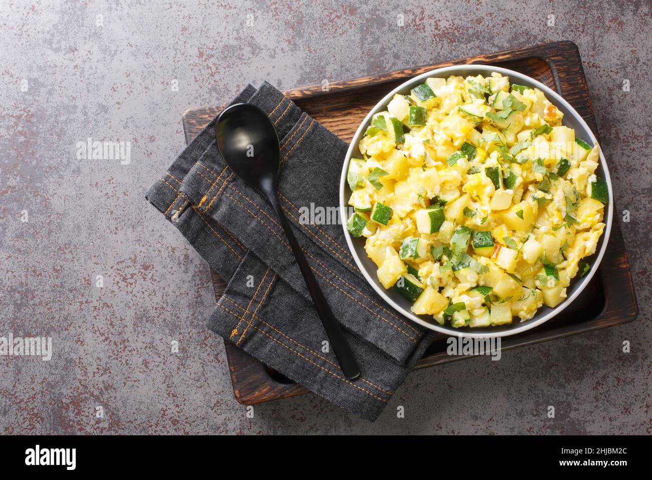 Spanische Rühreier mit Zucchini-Zwiebel und Kartoffeln in der Nähe auf dem Teller auf dem Tisch. Horizontale Draufsicht von oben Stockfoto