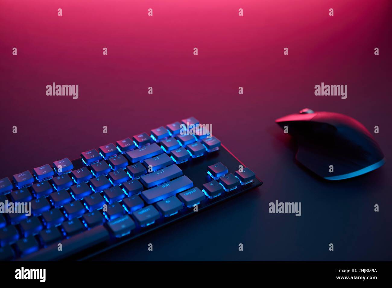 Blickfeld der blauen hinterleuchteten Tastatur und Maus auf dem Schreibtisch. Violettes Licht von oben. Professionelle Computerspiel spielen, eSport Business und Stockfoto