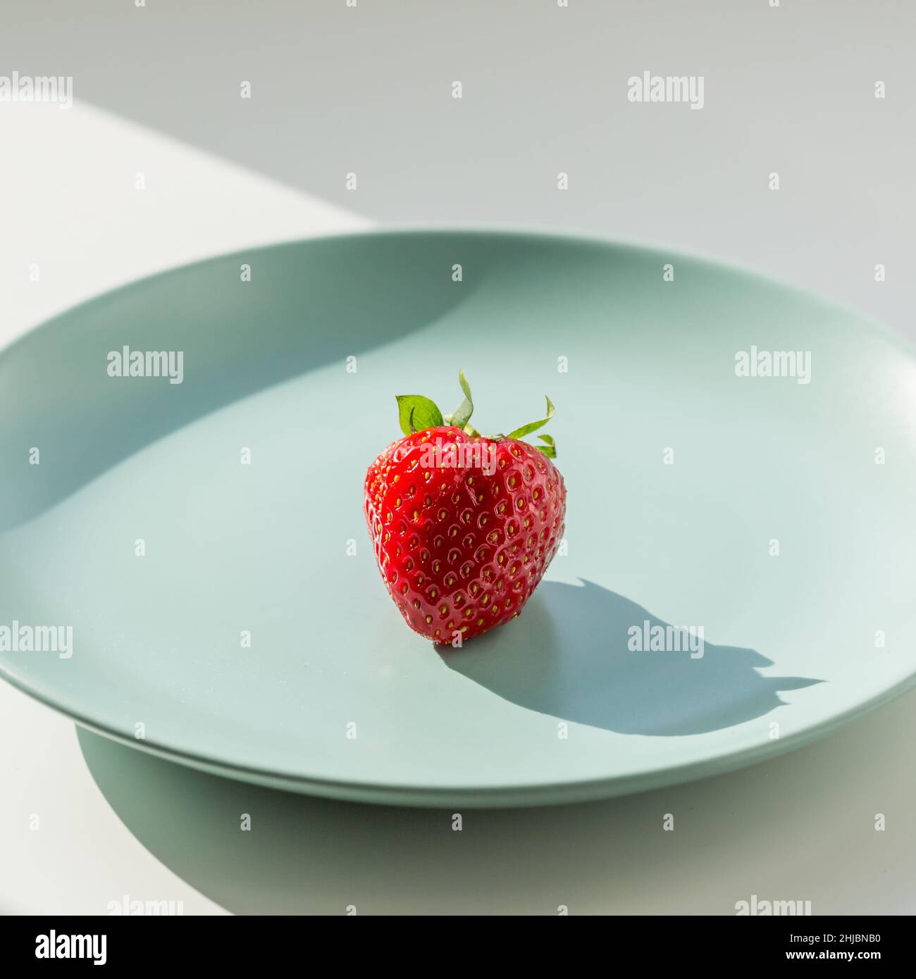 Eine rote Erdbeere auf dem grünen Teller. Gesundes Lifestyle-Konzept. Stockfoto