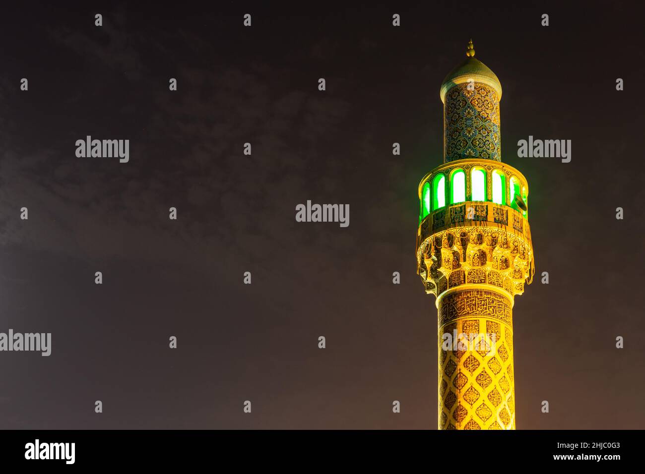 Beleuchtetes Minarett der iranischen Moschee (Imam Hussein Moschee) in Dubai, farbenfrohe Fassade aus persischen Fliesen mit orangefarbenen, gelben Steinen. Stockfoto