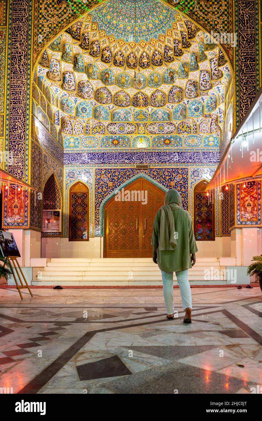 Muslimische Frau, die die iranische Moschee (Imam Hussein Moschee) in Dubai mit farbenfroher Fliesenfassade und persischer Architektur betreten hat. Stockfoto