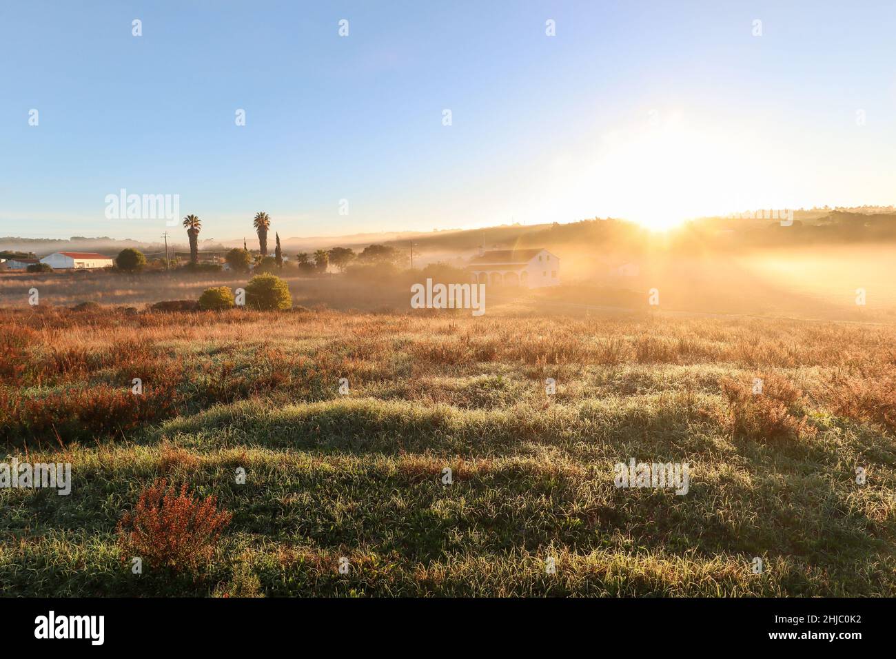 Blick auf die typische Alentejo-Landschaft mit portugiesischem Dorf im Morgennebel und aufgehender Sonne auf dem Wanderweg Rota Vicentina in der Nähe von Carrascalinhino, Aljezur Stockfoto