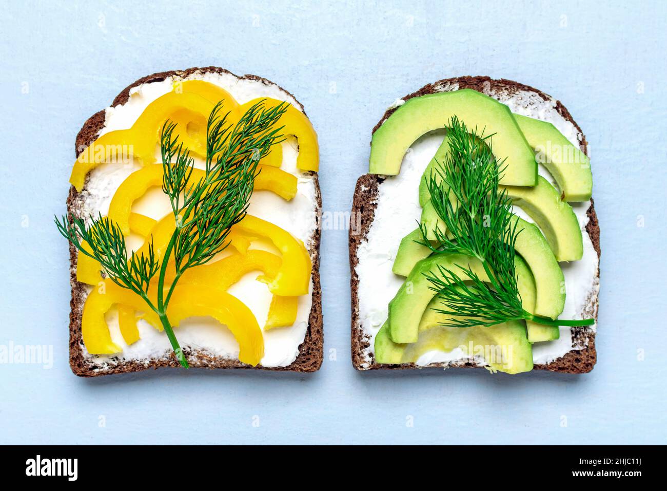 Verschiedene Sandwiches zum Frühstück - Scheibe Vollkornbrot, gelbe Paprika, Frischkäse, Avocado, garniert mit grünem Dill auf Blau Stockfoto