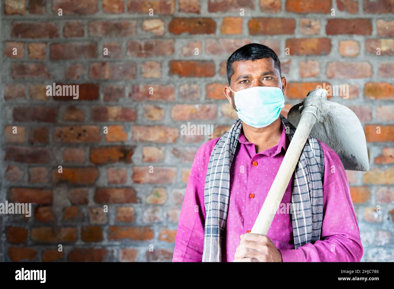 Selbstbewusster Bauarbeiter mit einer medizinischen Gesichtsmaske, die Kamera am Arbeitsplatz sieht – Konzept der Rückkehr zur Arbeit nach einer Coronavirus-Covid-19-Pandemie Stockfoto