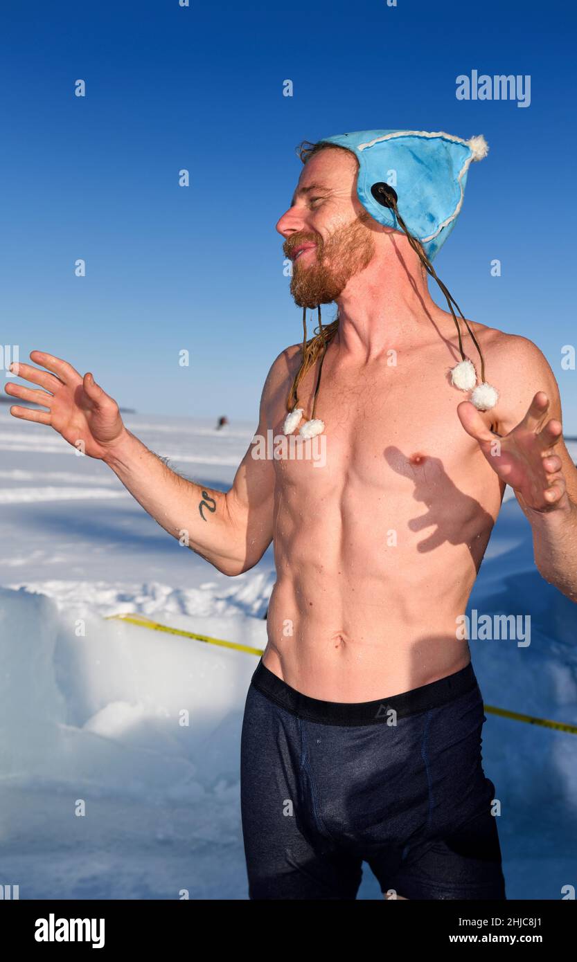 Nasser Mann im Hut, der nach einem kalten Wasser im Winter im Eiswasser in der Sonne am Kempenfelt Bay Lake Simcoe Barrie Ontario redet Stockfoto