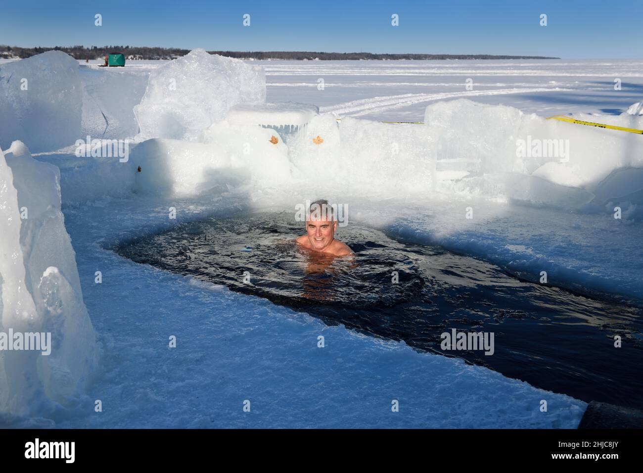 Mann in der Sonne schwimmt in einem Eisloch für ein kaltes Wasser schwimmen im Winter am Kempenfelt Bay Lake Simcoe Barrie Ontario Stockfoto