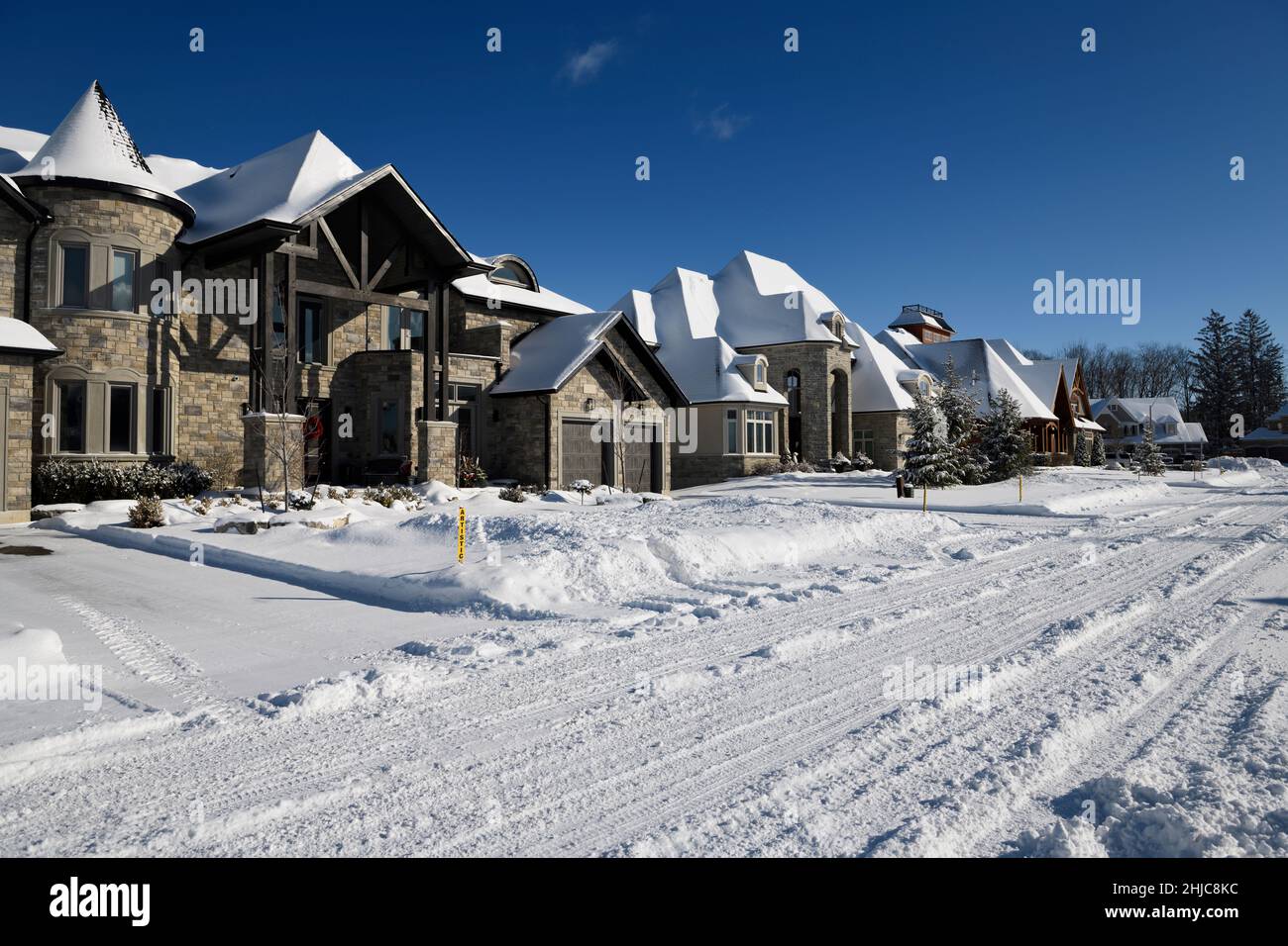 Neue große Häuser in der Sonne nach einem frischen Schneefall auf einer verschneiten Straße in Ontario, Kanada, überwintern mit blauem Himmel Stockfoto