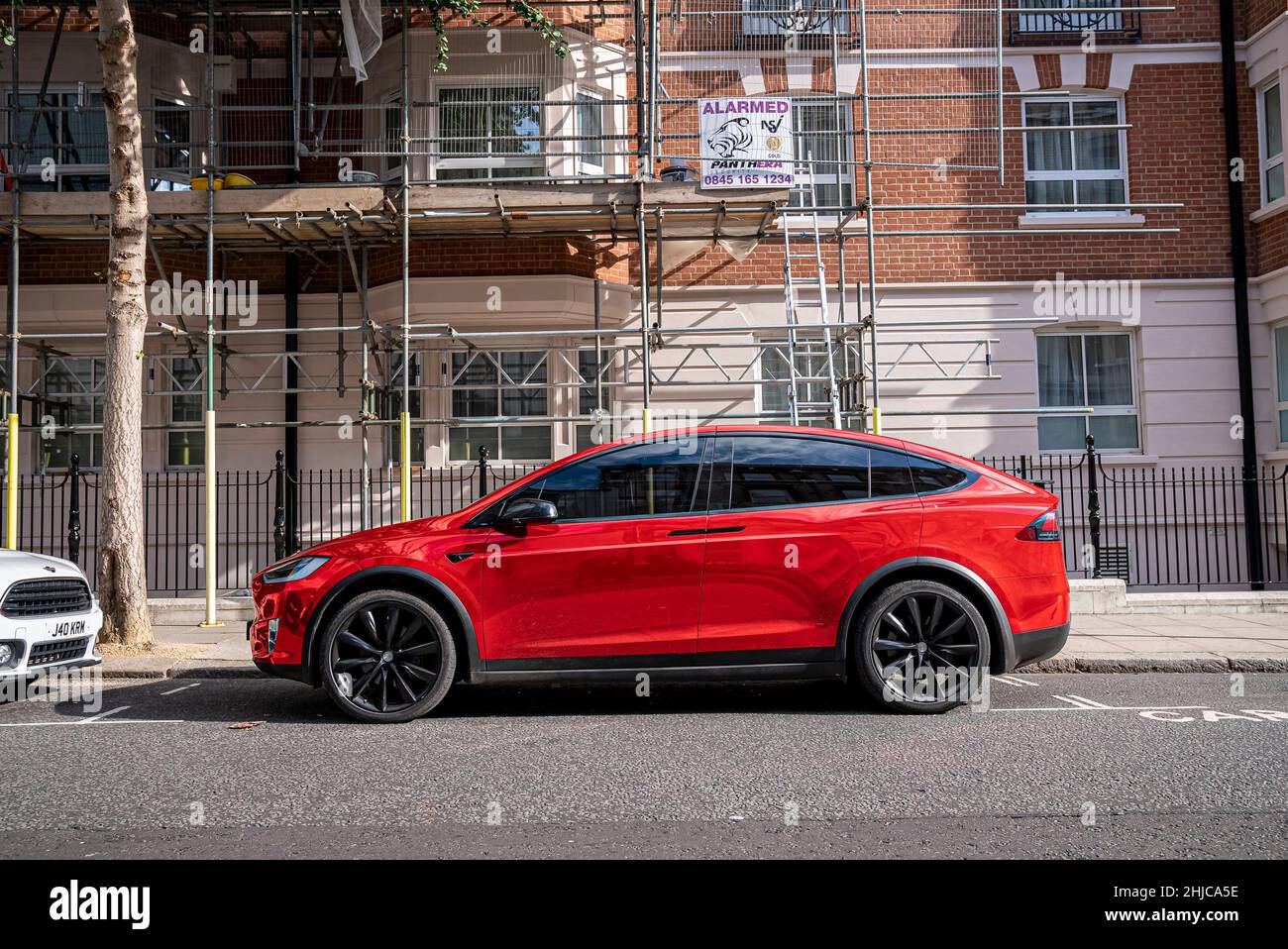 Rotes, modernes Tesla-Auto, das an der Straße in der Stadt durch Gebäude geparkt wurde Stockfoto