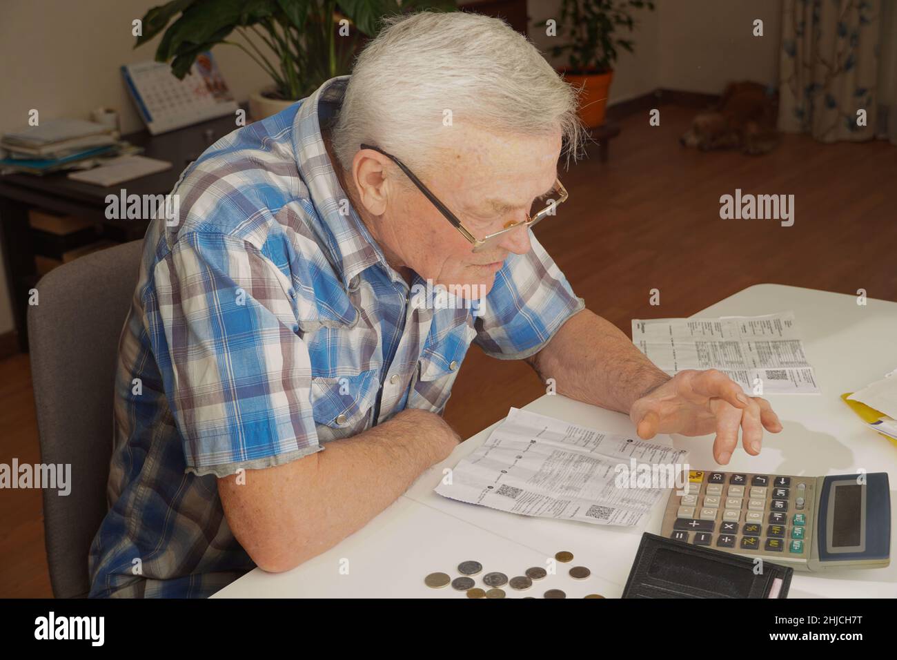 Älterer Mann, der am Tisch sitzt und die Finanzen berechnet. Alter Mann, der Rechnungen überprüft. Mann, der Münzen auf dem Tisch zählt. Pensionsberechnungskonzept Stockfoto