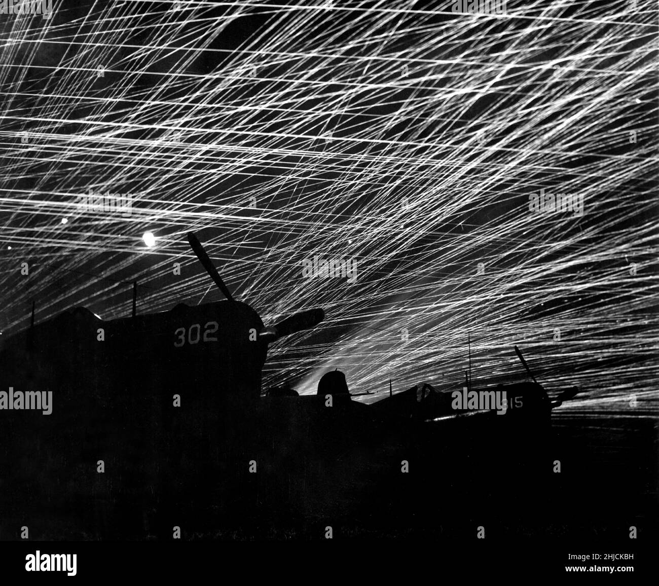Japanische Nachthemd-Raider werden von den Marine-Verteidigern des Flugplatzes Yontan auf Okinawa mit einem Luftabwehrfeuer begrüßt. Im Vordergrund stehen die marinen Kampfflugzeuge der Staffel „Hell's Belles“. Ca. 1945. Stockfoto