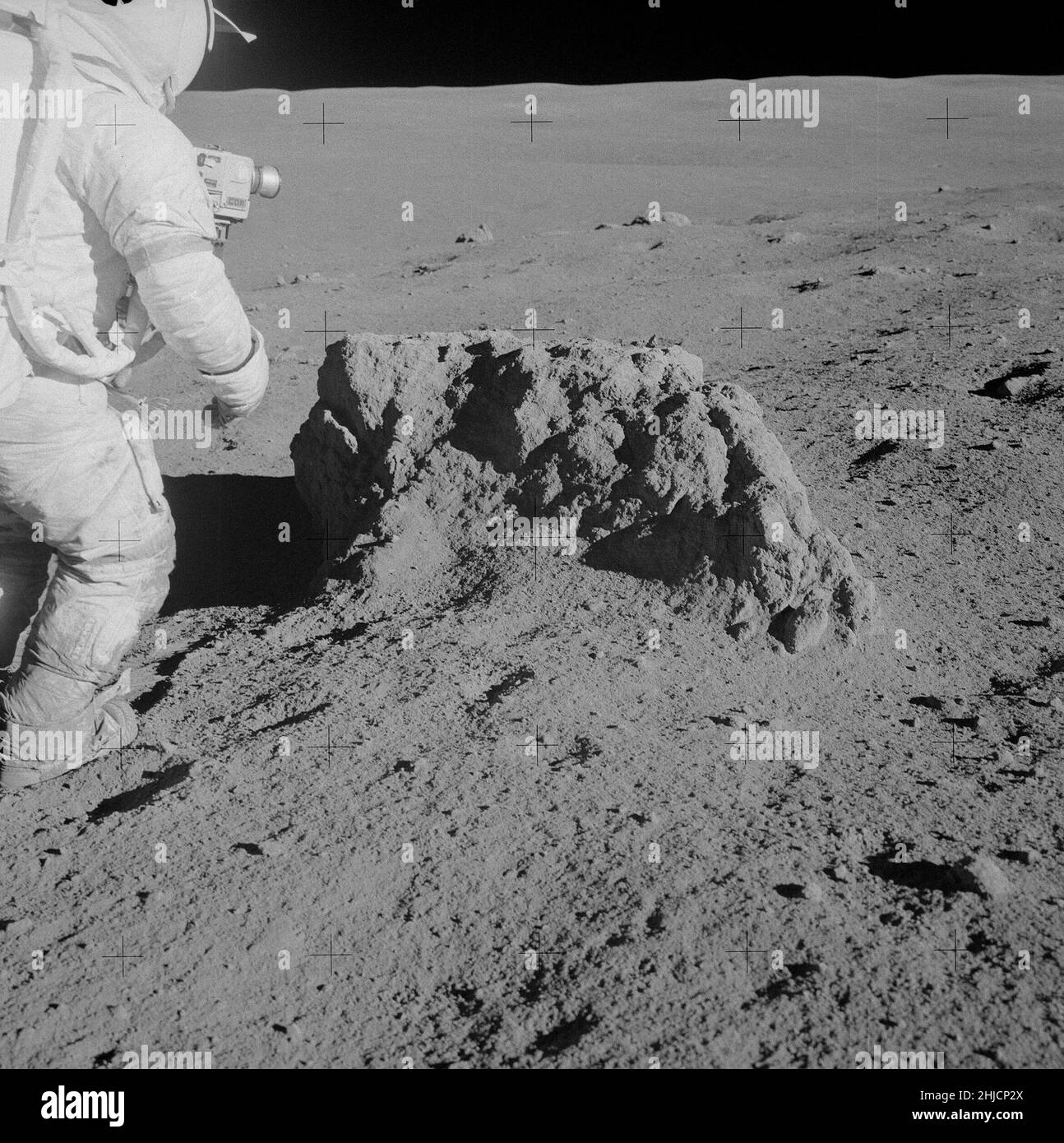 Apollo 14-Mission. Astronaut Alan Shepard neben dem Felsbrocken an Station B2. Im Apollo 14 Preliminary Science Report wird dieser Felsbrocken als Big Rock bezeichnet. Die obere Fläche ist ungewöhnlich flach und kann eine Bruchfläche darstellen. Der Fels ist 0,6 Meter hoch und etwa 1,5 Meter lang. Wir können Shepards Kamera mit CDR (Commander) auf der Seite sehen, die Zange unter seinen Schläuchen. Beachte den Schmutz auf seinen Stiefeln und Knien. Das Bild wurde in Richtung Norden aufgenommen. Shepard und Mitchell sind einen kleinen Anstieg hinaufgekommen und in der Ferne hinter dem Felsbrocken können wir einen großen Krater sehen. Stockfoto
