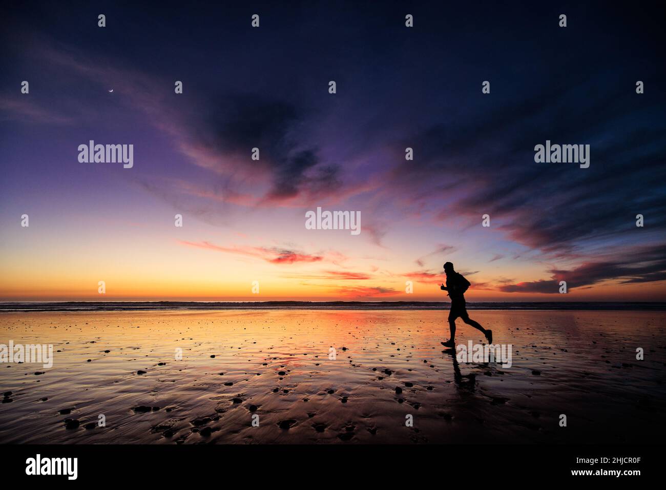 Ein Läufer spiegelte sich an einem glänzenden Strand unter einem farbenfrohen Winteruntergang am Torrey Pines State Beach wider. Stockfoto