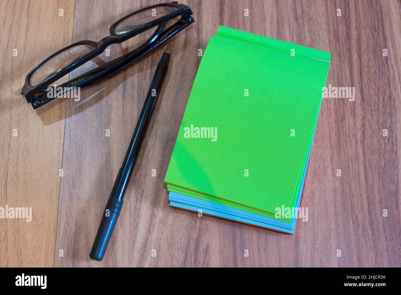 Farbiger Notizblock mit Lesebrille und Stift auf Holzschreibtisch. Flach liegend Stockfoto