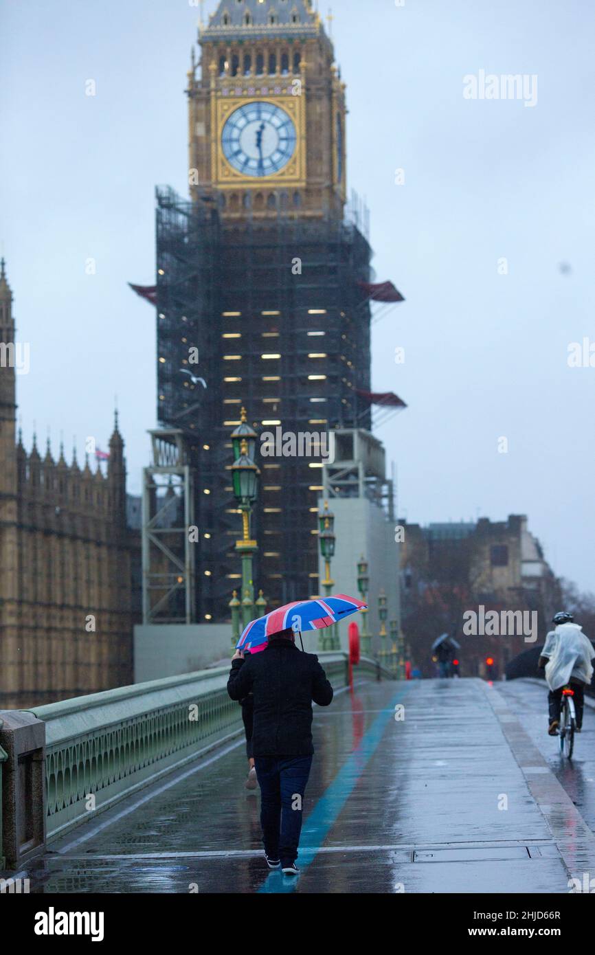 Der Elizabeth Tower, der gemeinhin als Big Ben bekannt ist, wird als Fußgänger angesehen, der einen Regenschirm mit der Unionsflagge auf der Westminster Bridge im Zentrum Londons hält. Stockfoto