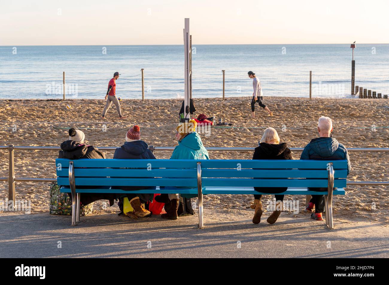Menschen, die auf einer Bank sitzen und ein Strandvolleyball-Spiel beobachten Stockfoto
