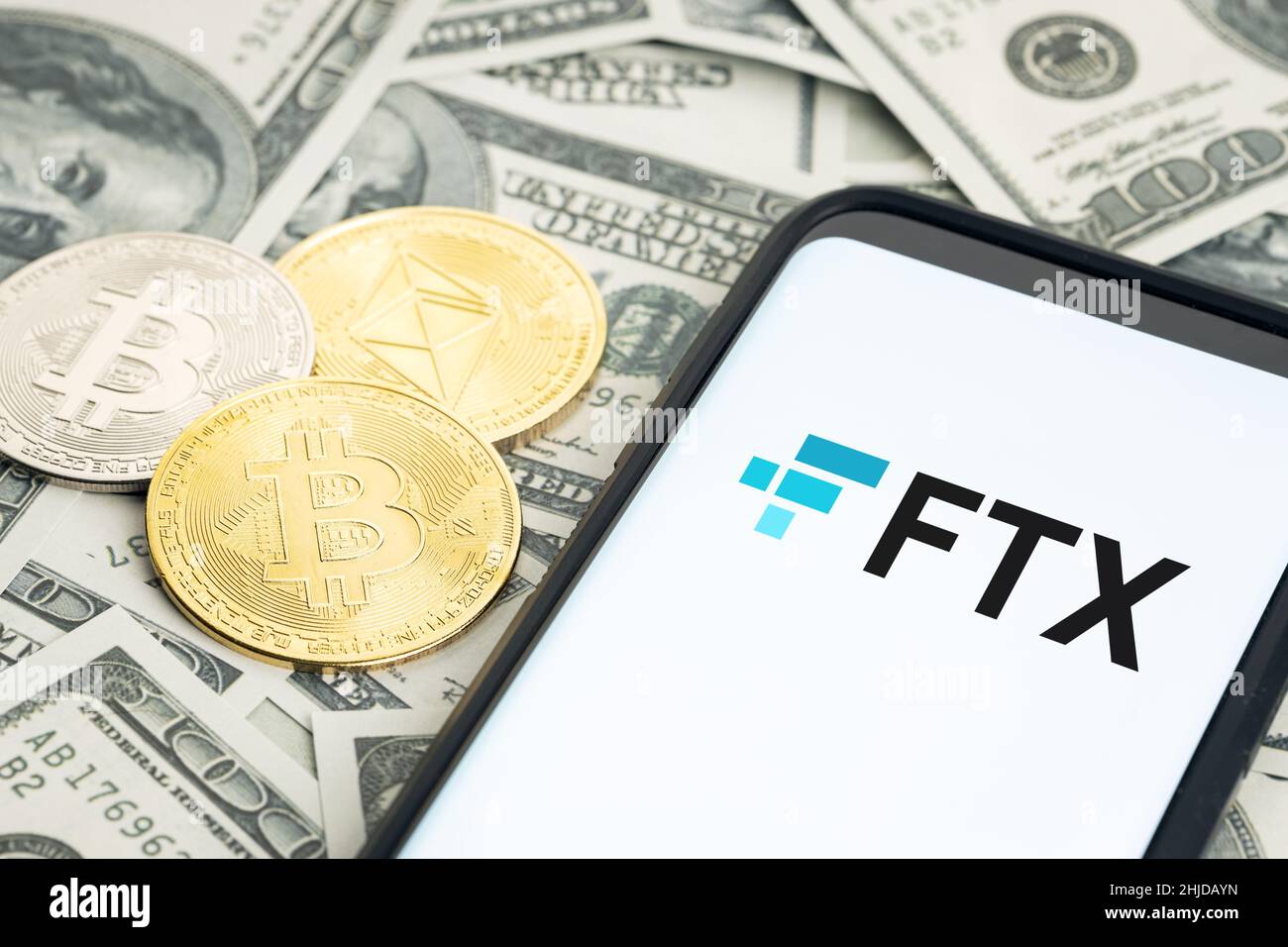 Galicia, Spanien; 28. januar 2022: FTX-Logo auf Smartphone-Bildschirm und Dollar-Banknoten sowie Bitcoin- und ethereum-Münzen Stockfoto