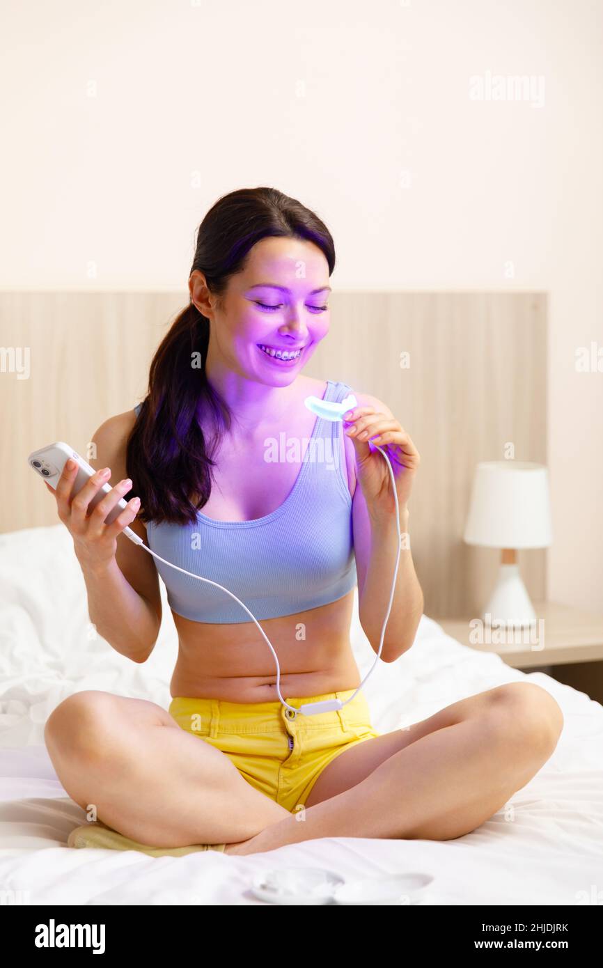 Eine junge Frau verwendet einen Aufhellungskomplex für die Zahnaufhellung zu Hause. USB-UV-Lampe für Zahnaufhellung Stockfoto