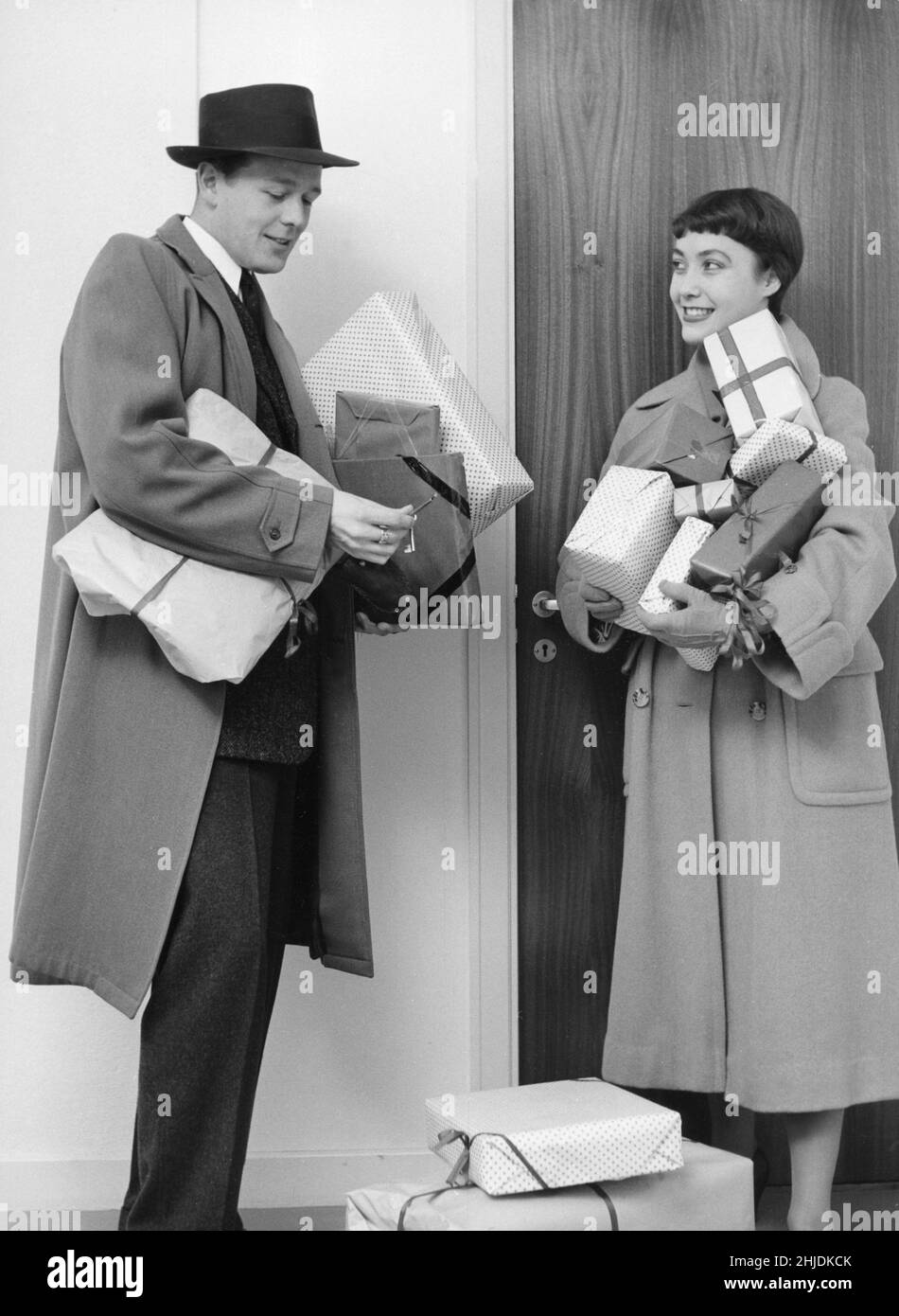 Weihnachten im Jahr 1950s. Ein Paar mit weihnachtsgeschenken nach einer Einkaufstour, das zu seinem Haus zurückkehrt und sich ein wenig mit dem Schlüssel zur Tür kämpft. 1953 Stockfoto