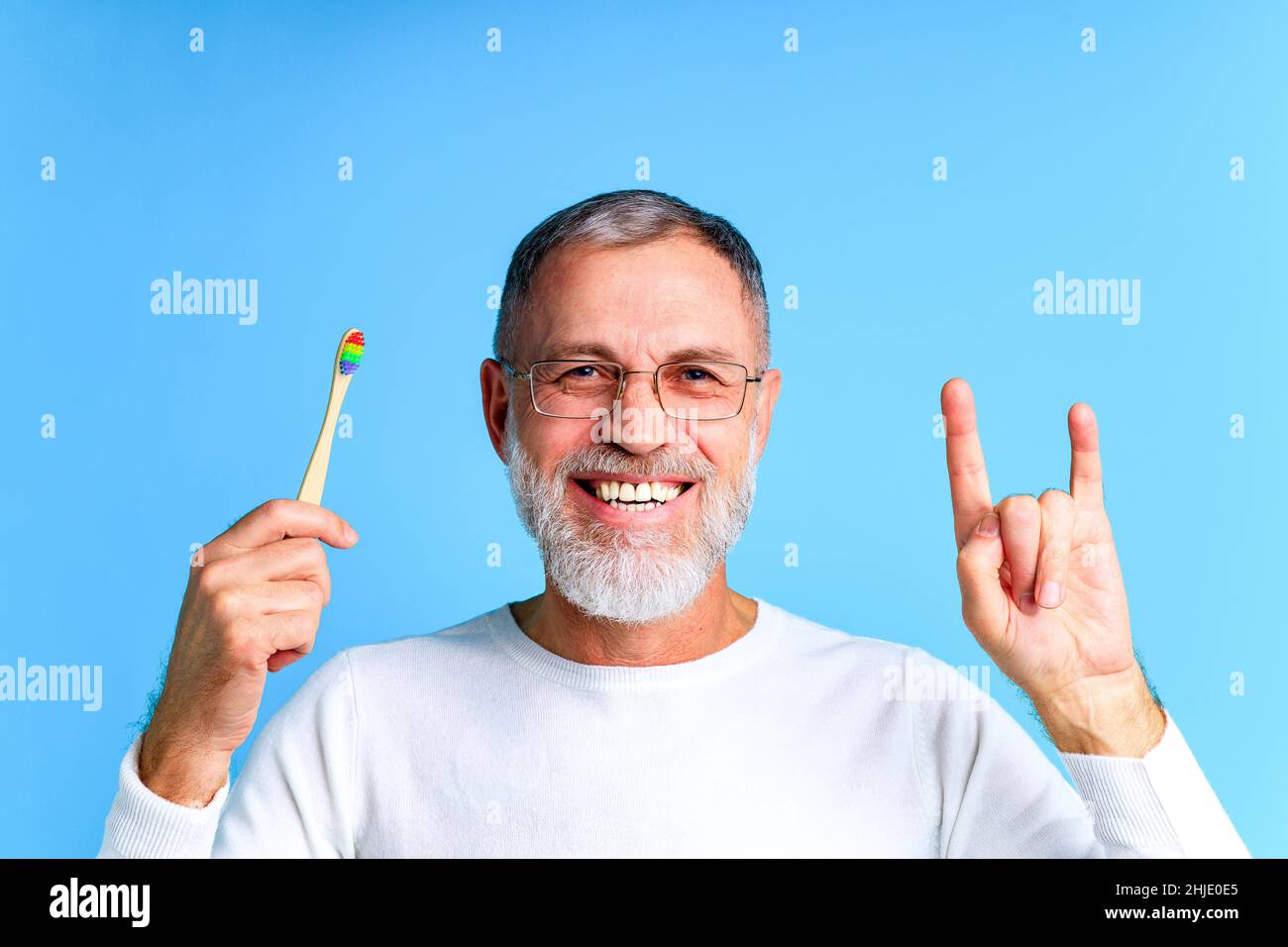 Mann zeigt mehrfarbige Regenbogen Zahnbürste in blauem Hintergrund Studio Stockfoto