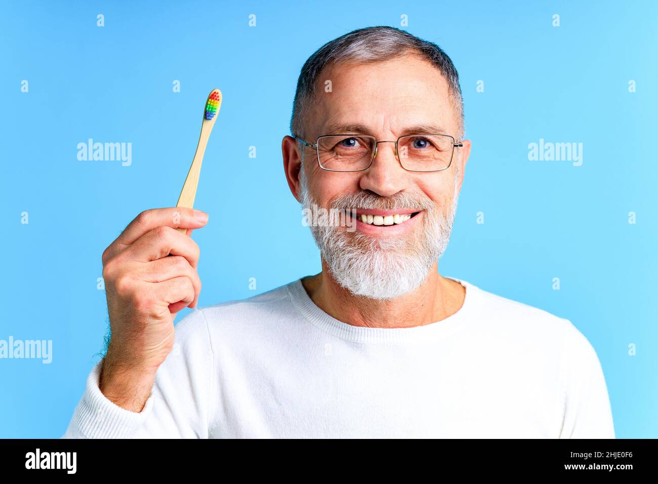 Mann zeigt mehrfarbige Regenbogen Zahnbürste in blauem Hintergrund Studio Stockfoto