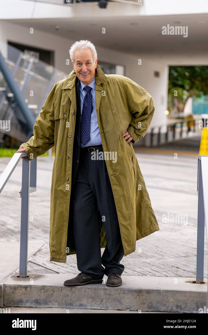 Ein gutaussehender, lächelnder Geschäftsmann trägt einen Trenchcoat über seinem Anzug Stockfoto