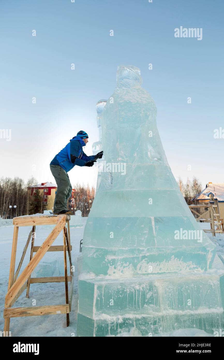 Der Bildhauer schneidet aus einem Eisblock eine Eisfigur mit einem Meißel zu WEIHNACHTEN auf einem Holzgerüst Stockfoto