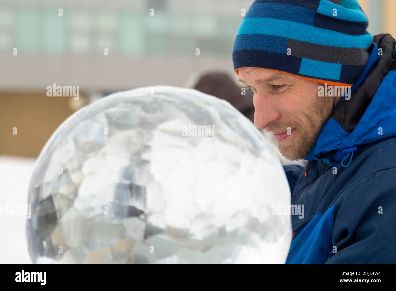 Ein Bildhauer schnitzt mit einem Meißel eine runde Eiskugel aus einem Eisblock. Stockfoto