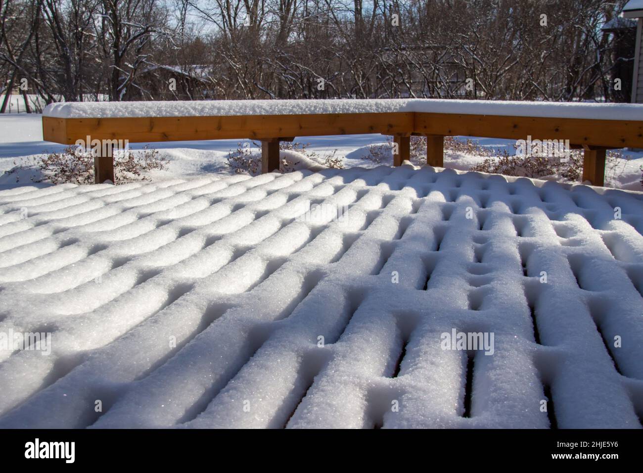 Im Winter mit natürlichem Sonnenlicht können Sie auf einer Holzterrasse und -Bank frische Schneedesigns im Freien betrachten Stockfoto