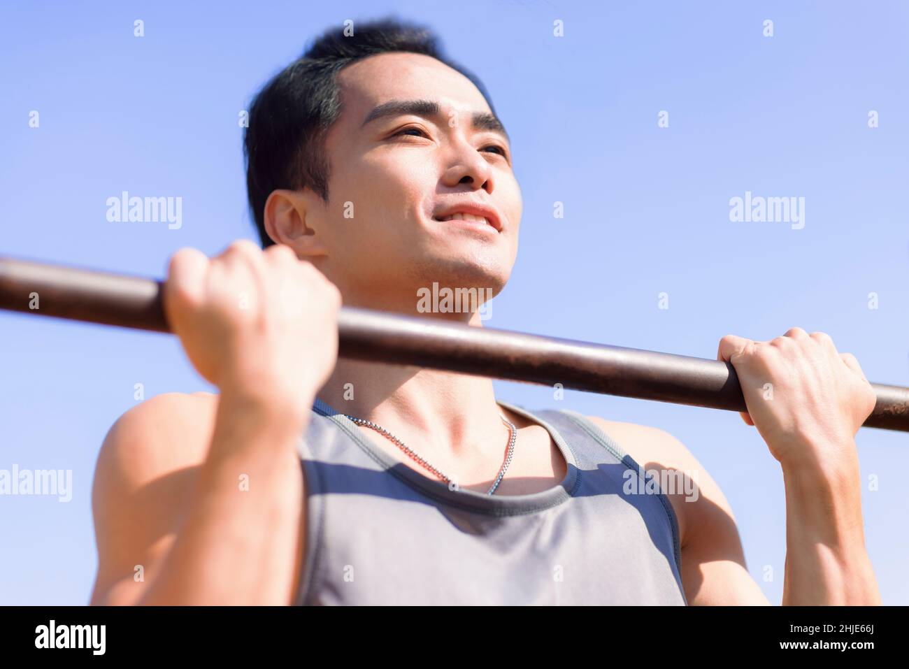 Junger Mann, der draußen trainiert und seinen Oberkörper über den horizontalen Balken hält Stockfoto