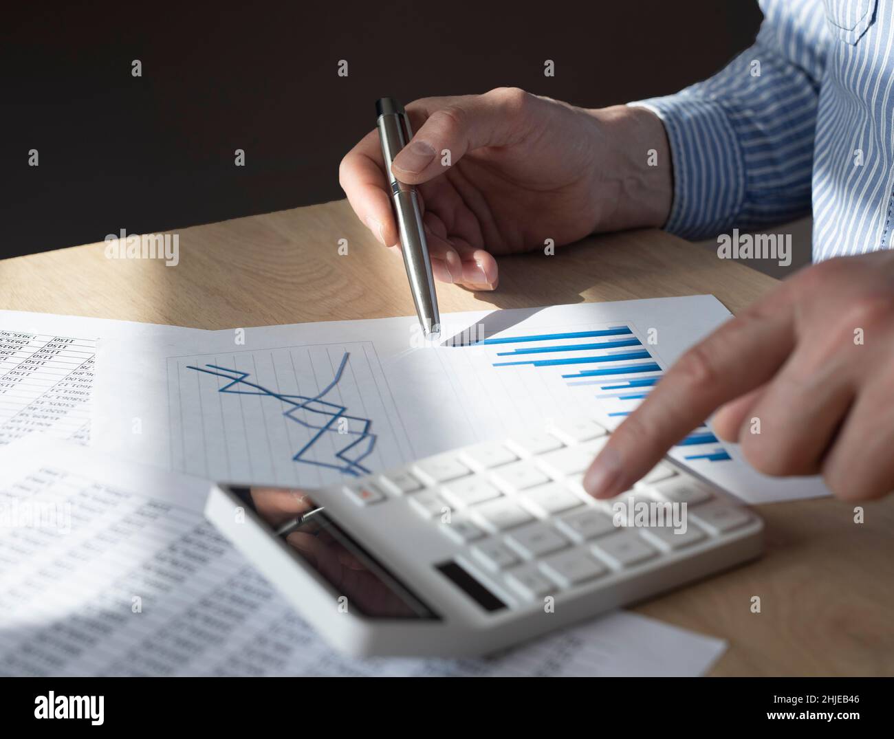 Männliche Hand am Schreibtisch mit Finanzdokument mit Diagramm des wachsenden Trends, Berechnungen, Berichtsvorbereitung. Konzept des Wirtschaftswachstums. Stockfoto