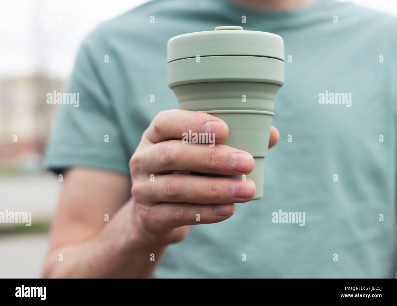 Wiederverwendbarer Eco-Becher zum Mitnehmen von Kaffee oder Tee. Männliche Hand mit nachhaltigem Silikonbecher. Umweltfreundliche Person leben. Stockfoto