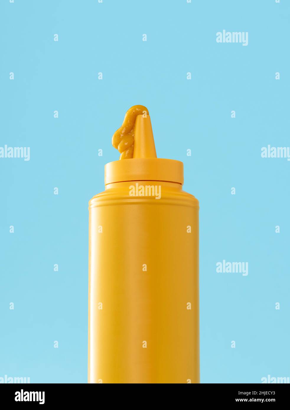 Nahaufnahme mit gelber Senfflasche vor blauem Hintergrund. Ein Tropfen Senf oben auf der Flasche. Gelbe Kunststoffflasche isoliert auf b Stockfoto