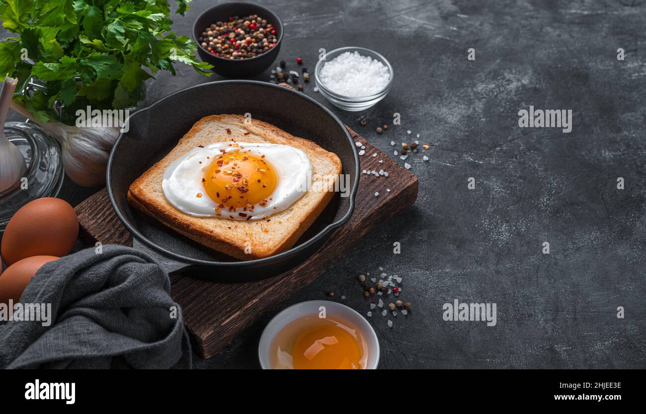 Gebratener Toast mit einem Ei in einer Pfanne auf dunklem Grund. Seitenansicht, Kopierbereich. Stockfoto