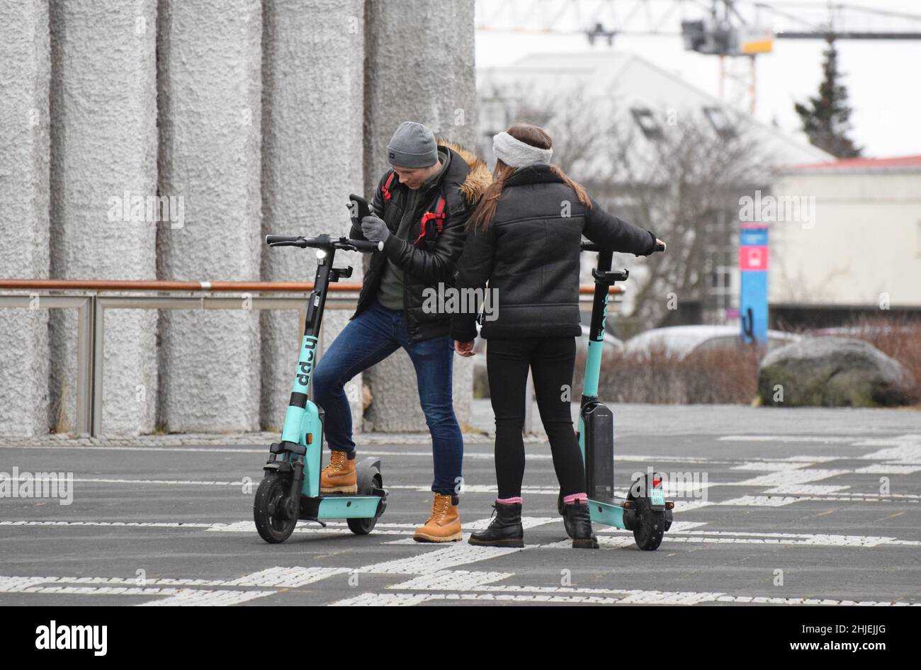 Ein junges Paar, das im Januar 2022 in Reykjavík Island Urlaub macht und 2 E-Scooter auf dem Platz vor der Kathedrale von Hallgrímskirkja mietet Stockfoto