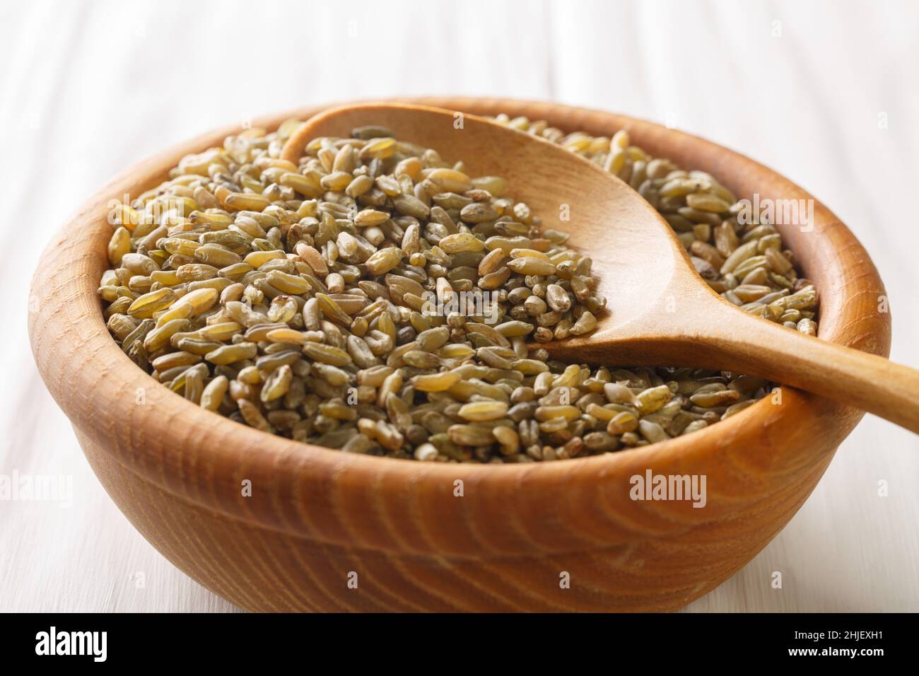Bio Roh Cracked Wheat Freekah in einer Schüssel mit Holzlöffel auf weißem rustikalen Tisch. Horizontal Stockfoto