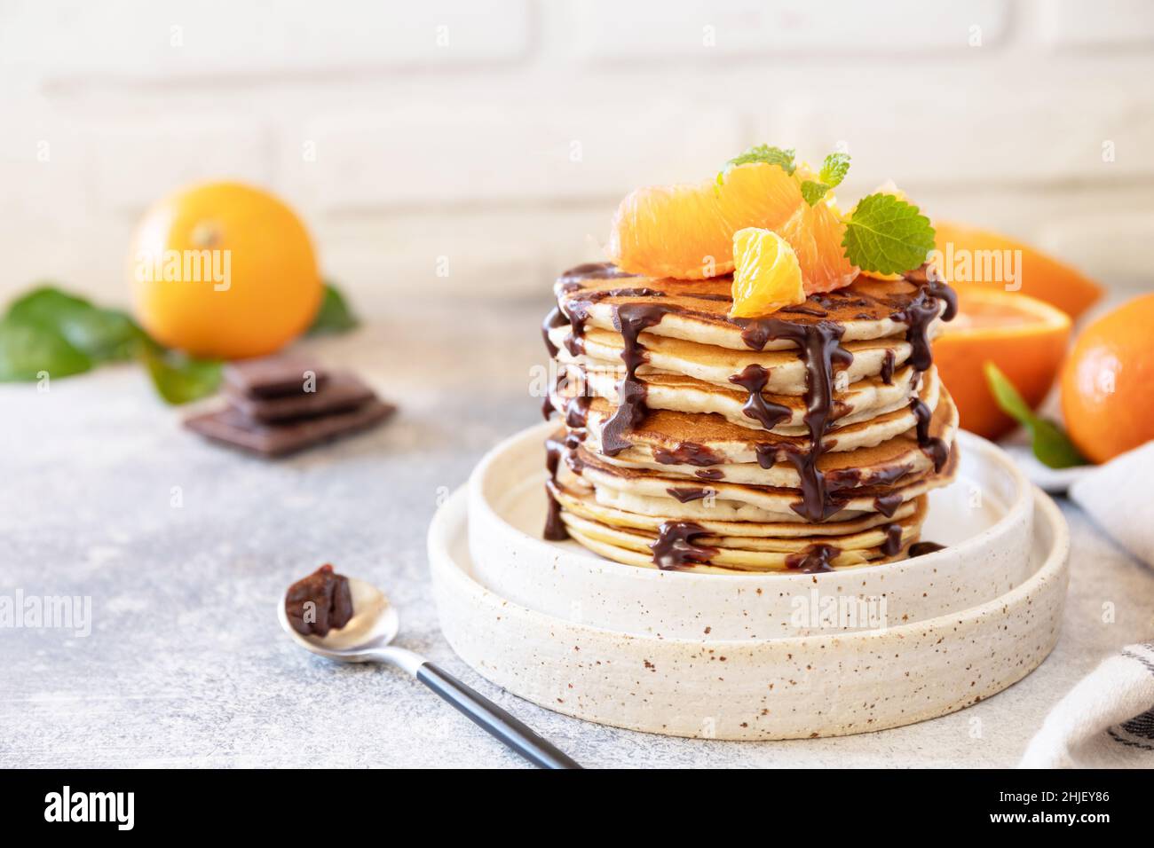 Wir feiern den Pfannkuchen-Tag, ein gesundes Frühstück. Köstliche hausgemachte pfannkuchen mit amerikanischen Bananen mit Schokolade und roter Orange auf grauem Steingrund. Kopieren Stockfoto
