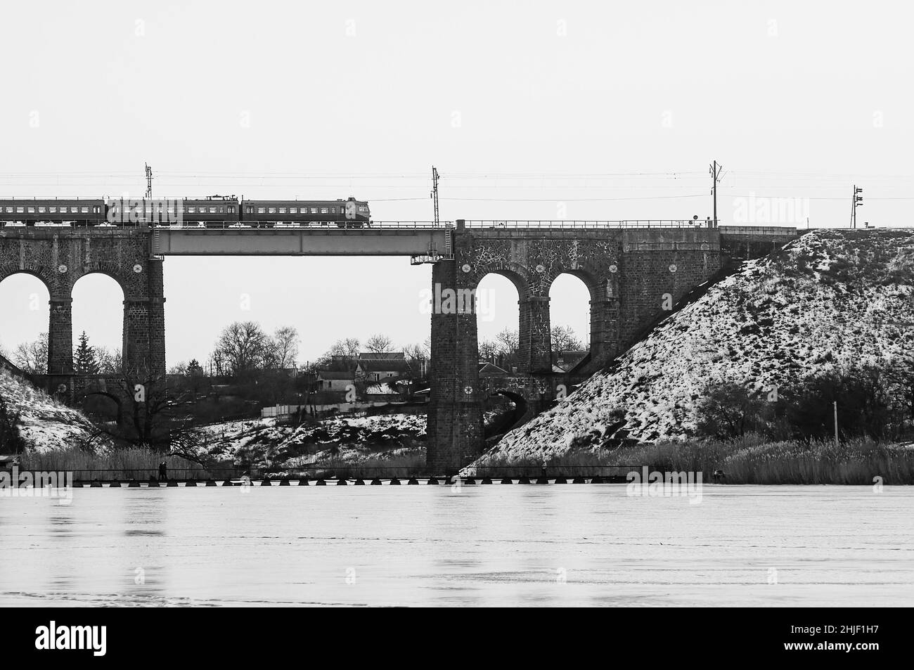 Zug auf einer hohen alten Brücke über den Fluss, Winter Fluss in Eis und Schnee. Steineisenbahn-Brücke mit Bögen, Viadukt in Kropyvnytskyi. Stockfoto