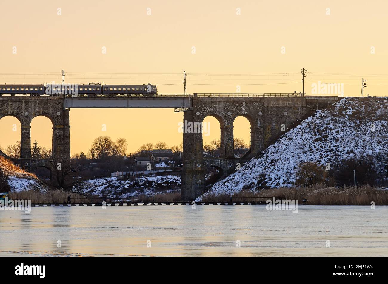 Zug auf einer hohen alten Brücke über den Fluss, Winter Fluss in Eis und Schnee. Steineisenbahn-Brücke mit Bögen, Viadukt in Kropyvnytskyi. Stockfoto