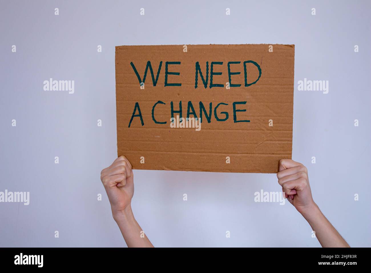 Handgehaltener Karton mit der Aufschrift „We need a change“ auf grauem Wandhintergrund. Sie kann gegen die globale Erwärmung oder Umweltverschmutzung protestieren. Stockfoto