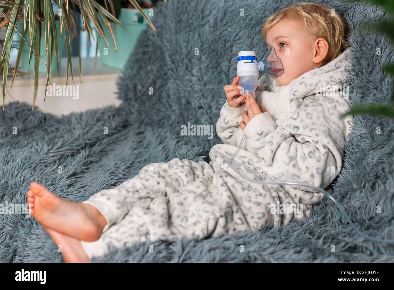 Niedlicher Baby Junge macht Inhalation mit einem Vernebler Ausrüstung. Krankes Kind, das den Inhalator in der Hand hält und zu Hause durch einen Inhalator atmet. Physische Stockfoto